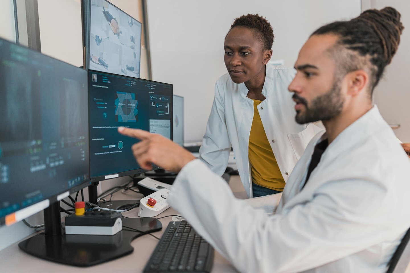 Two doctors in lab coats look at medical scans on computer screens.